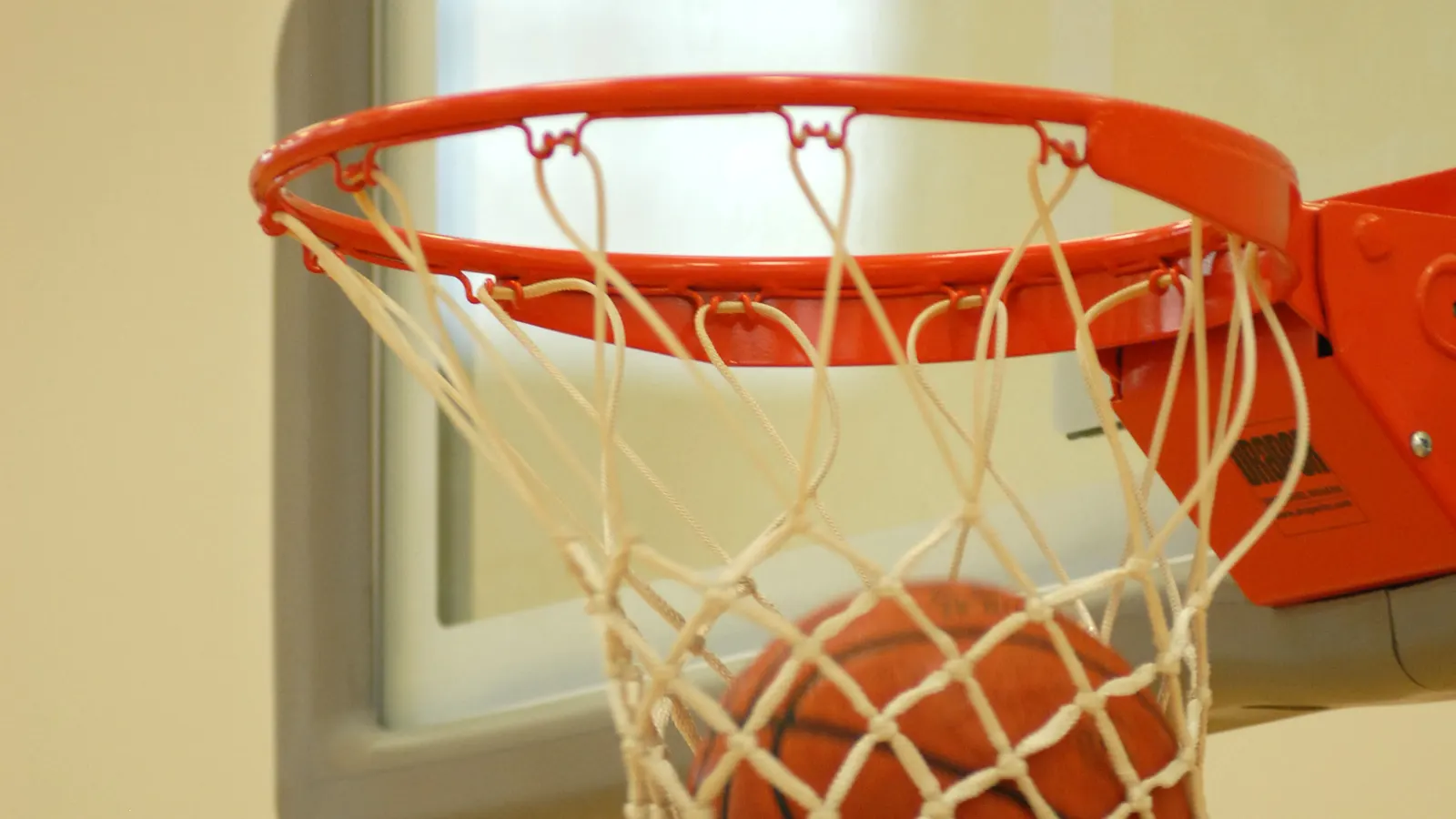 Ballon de basketball traversant un cercle rouge et son filet blanc dans un gymnase