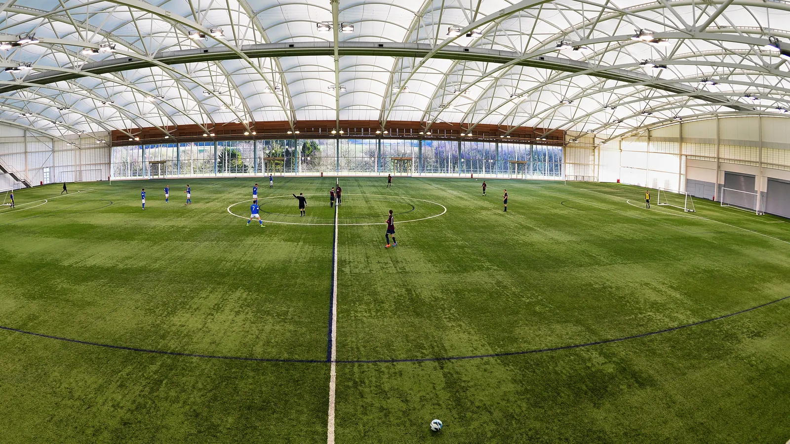 Match de football sur un terrain synthétique couvert, sous une grande structure blanche