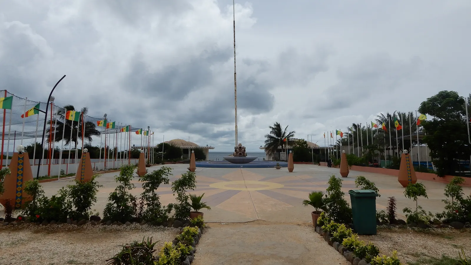Grande esplanade dallée à Dakar bordée de mâts avec des drapeaux du Sénégal, face à la mer
